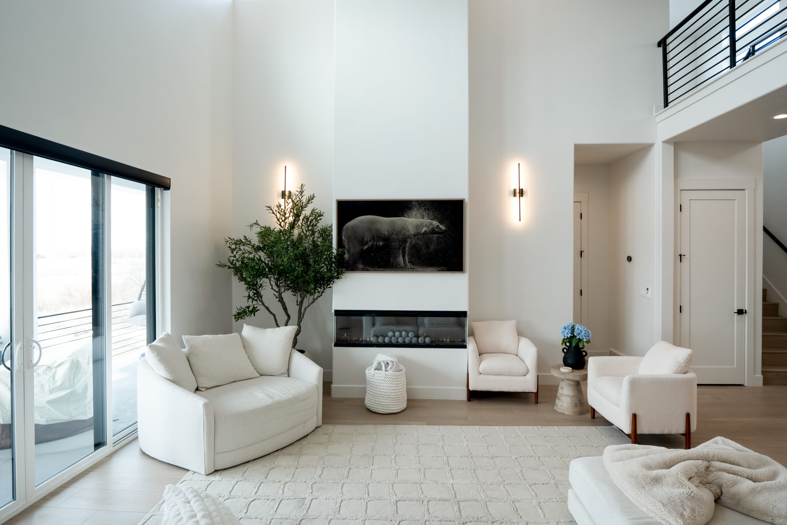High-ceilinged living room with fireplace, sliding glass doors, and mezzanine balcony.