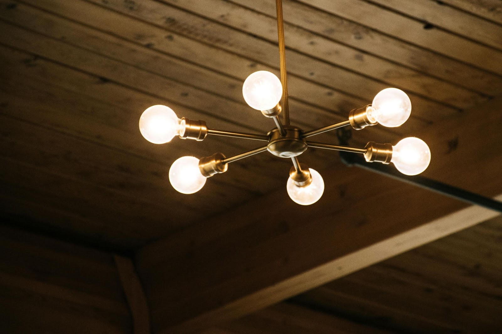 A mid-century modern chandelier with six exposed bulbs hangs from a wooden ceiling.