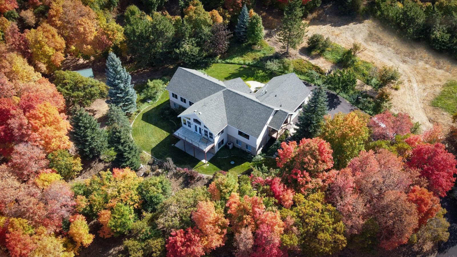 An aerial view shows a large house nestled among a forest of trees displaying brilliant red, orange, and yellow autumn foliage.