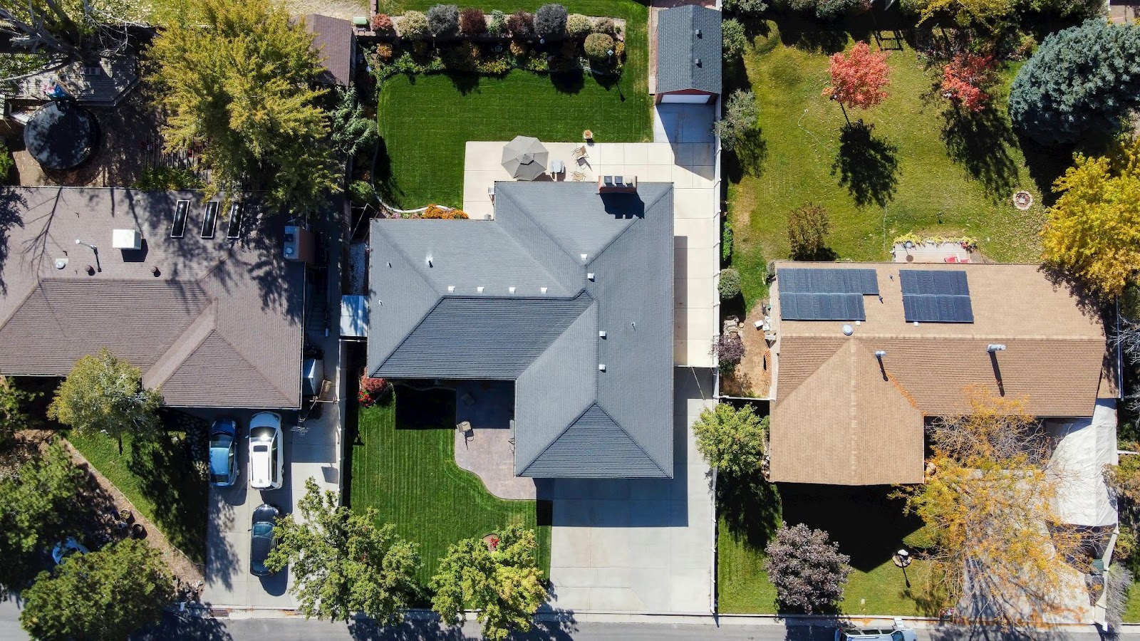 An aerial view of a suburban house with a light-colored tile roof shows several rectangular solar panels installed on different roof sections.