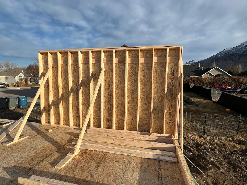 Wooden frame of a new home under construction in rural Utah at sunset, showing early building stages and open countryside.