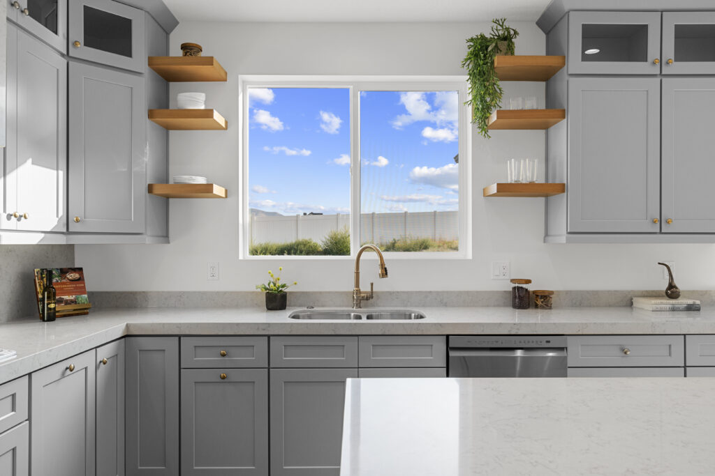Custom kitchen interior with gray cabinets, open wood shelving, white countertops, and large window view of Utah sky.
