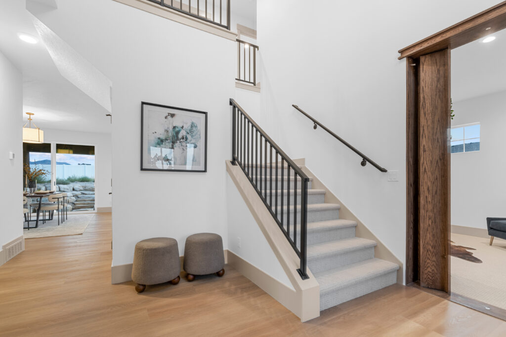 Bright entryway of a modern Utah home featuring wood floors, carpeted stairs, and open layout with natural light.