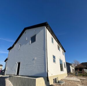 Completed two-story home with fresh siding and stucco foundation, showing the clean exterior finish of a custom Roots Builders project under clear blue skies in Utah.