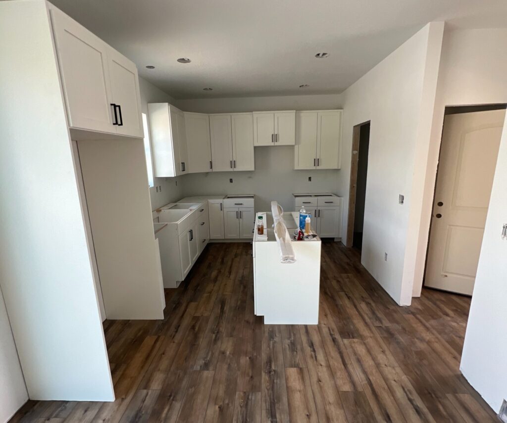 Bright modern kitchen under construction in a Roots Builders custom home, featuring white cabinetry and wood flooring.