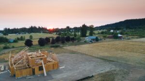 Aerial view of a new home under construction surrounded by Utah farmland and mountain horizon at sunrise.