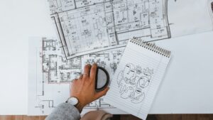 A person reviewing detailed architectural floor plans for a custom home with a notebook and coffee cup on the desk, symbolizing early design planning.