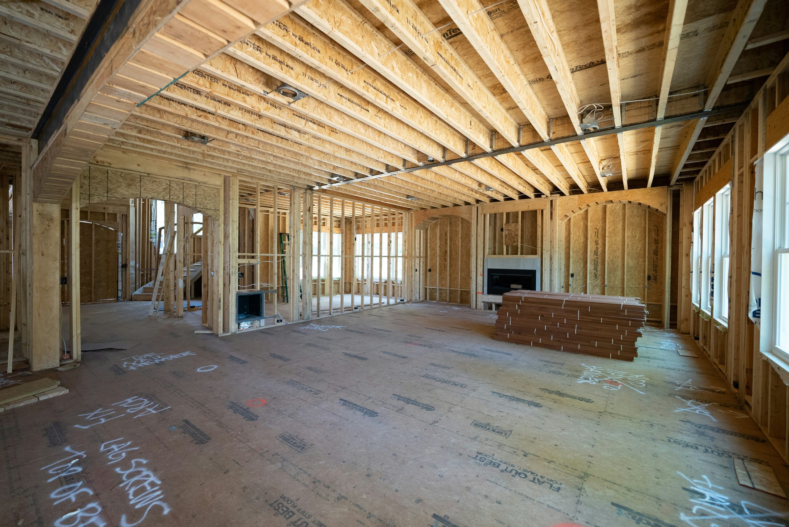 Framed interior of a new home under construction, showing wood beams, open layout, and natural light.