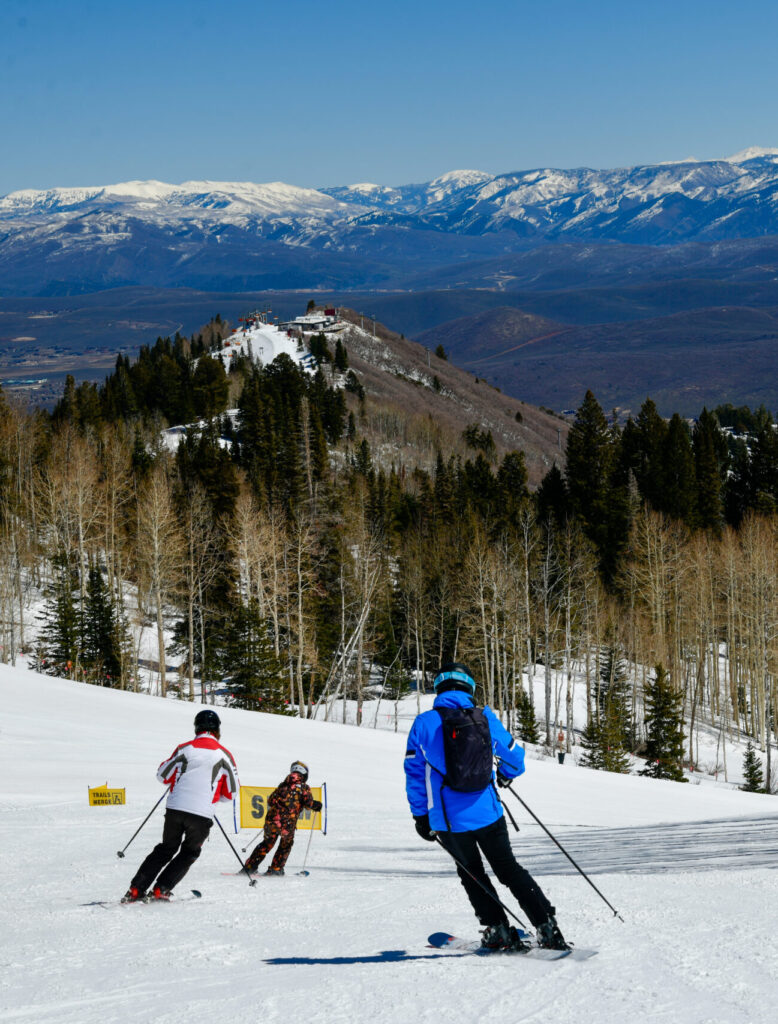 Skiers enjoying a sunny winter day at Deer Valley Resort in Park City, Utah, with snow-covered slopes, tall aspens, and mountain views in the distance.