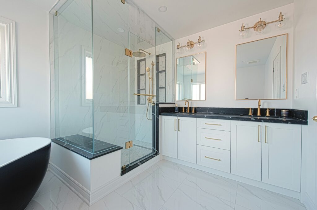 Modern bathroom remodel featuring a glass shower, double vanity, and gold fixtures.